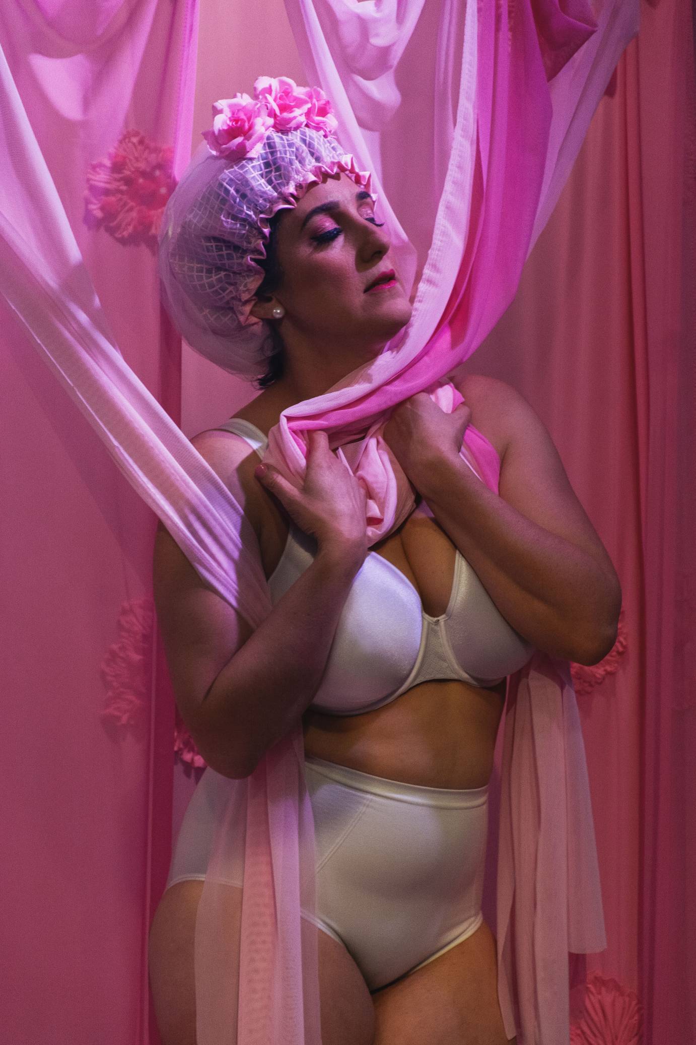 Sara Juli, in bra, panties, and shower cap, holds pink fabric to her chest